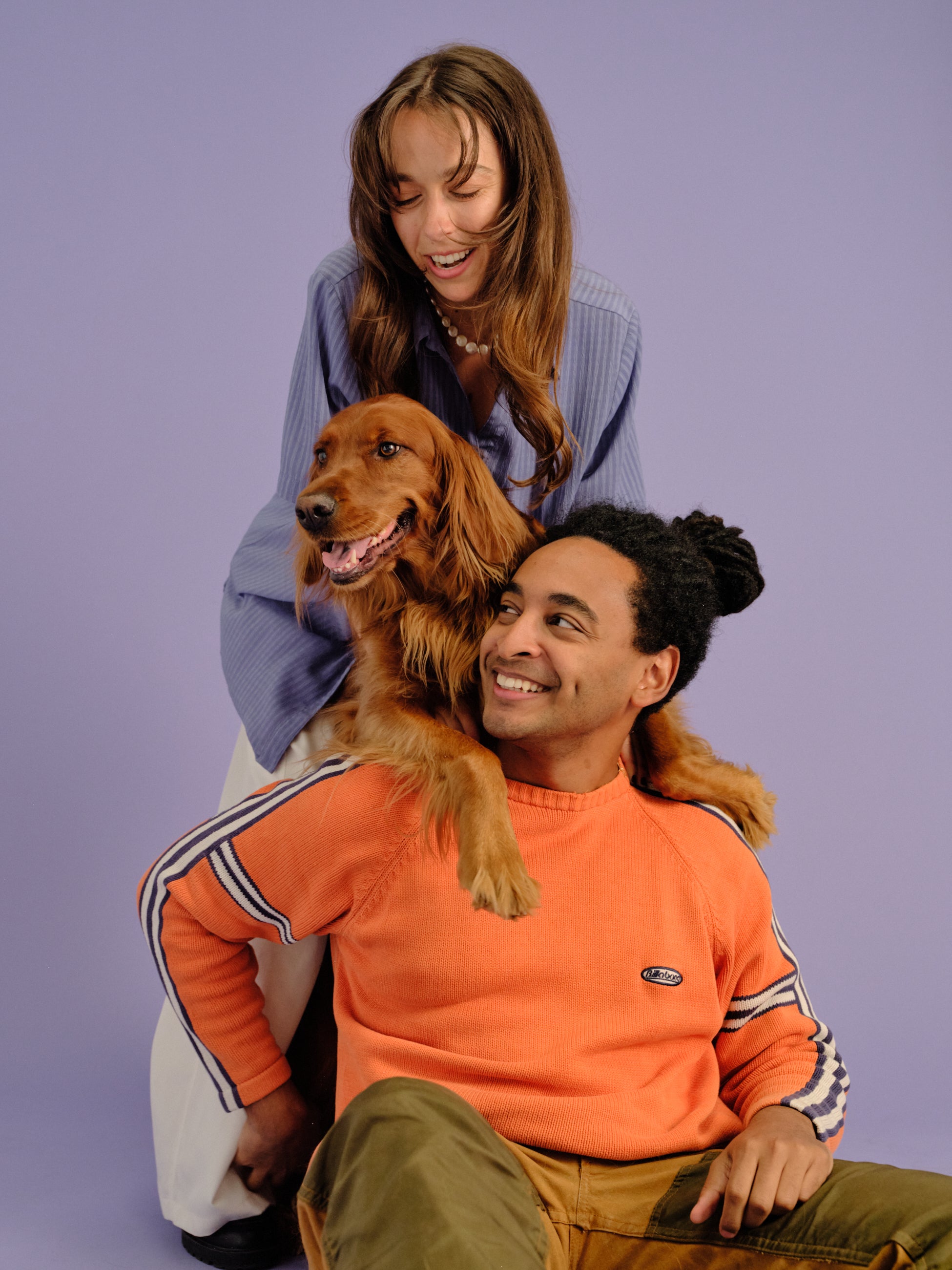A couple sitting down, looking happy with their golden retriever.